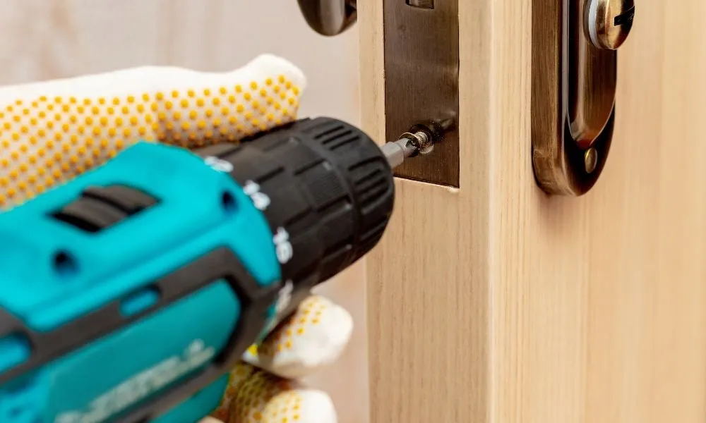 Gloved hand installing door lock with power drill