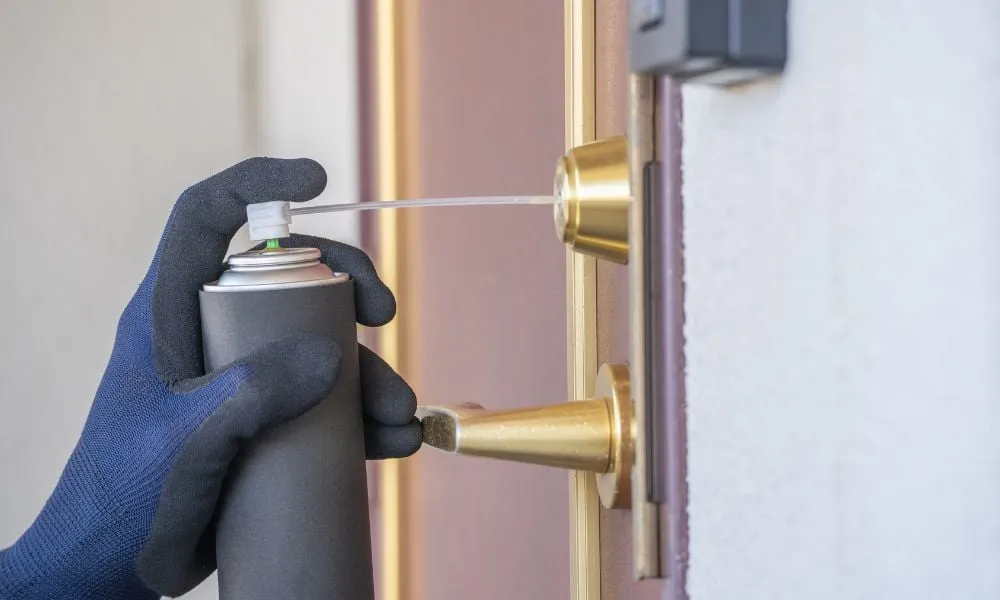 Gloved hand spraying lubricant into door lock