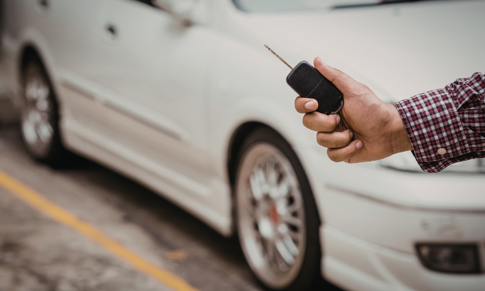 Hand holding car key fob near white car