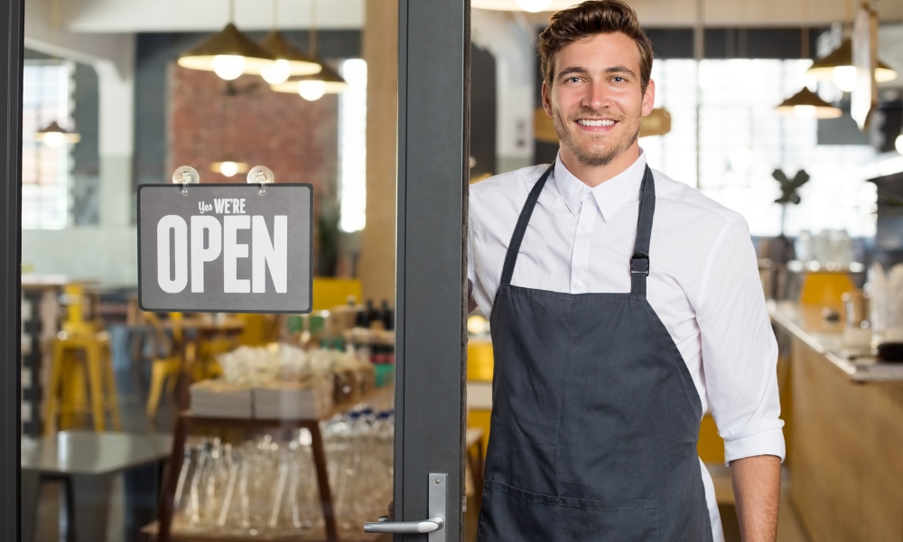Smiling café owner beside open shop sign
